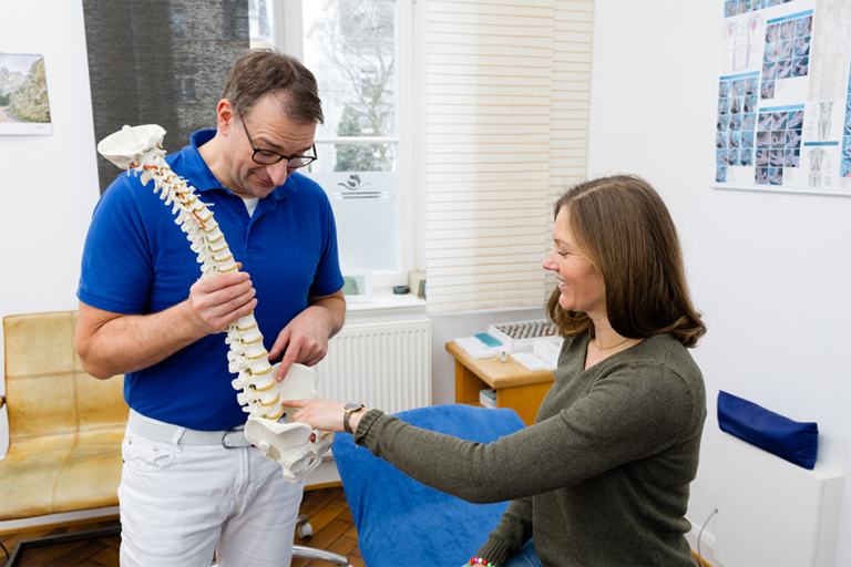 Dr. Marc Stracke zeigt einer Patientin ein Wirbelsäulenmodell.